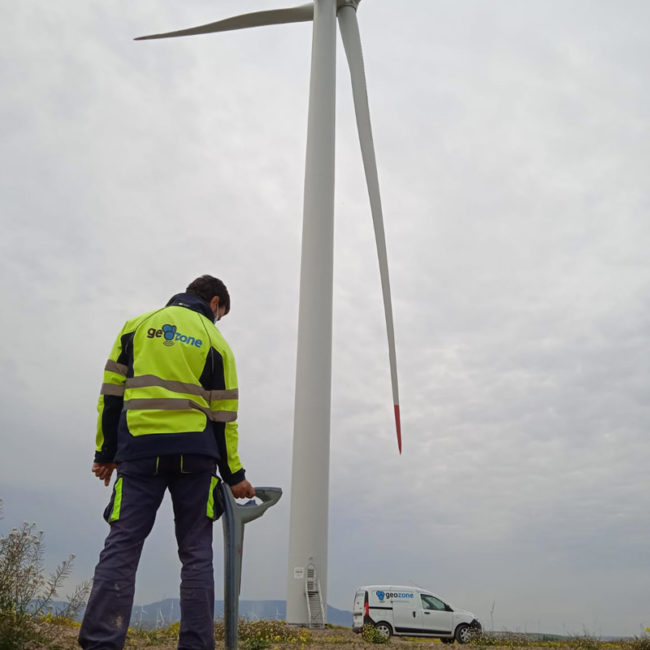 Técnico de Geozone realizando estudio geofísico en parque eólico junto a aerogenerador